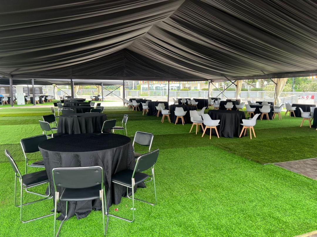 Black-lined marquee interior with round tables and black linens on green turf